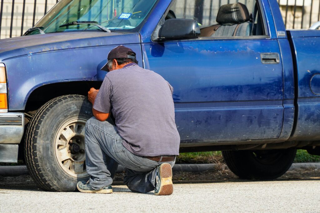 A man attentively repairing a flat tire on a blue truck in sunny Houston, Texas.