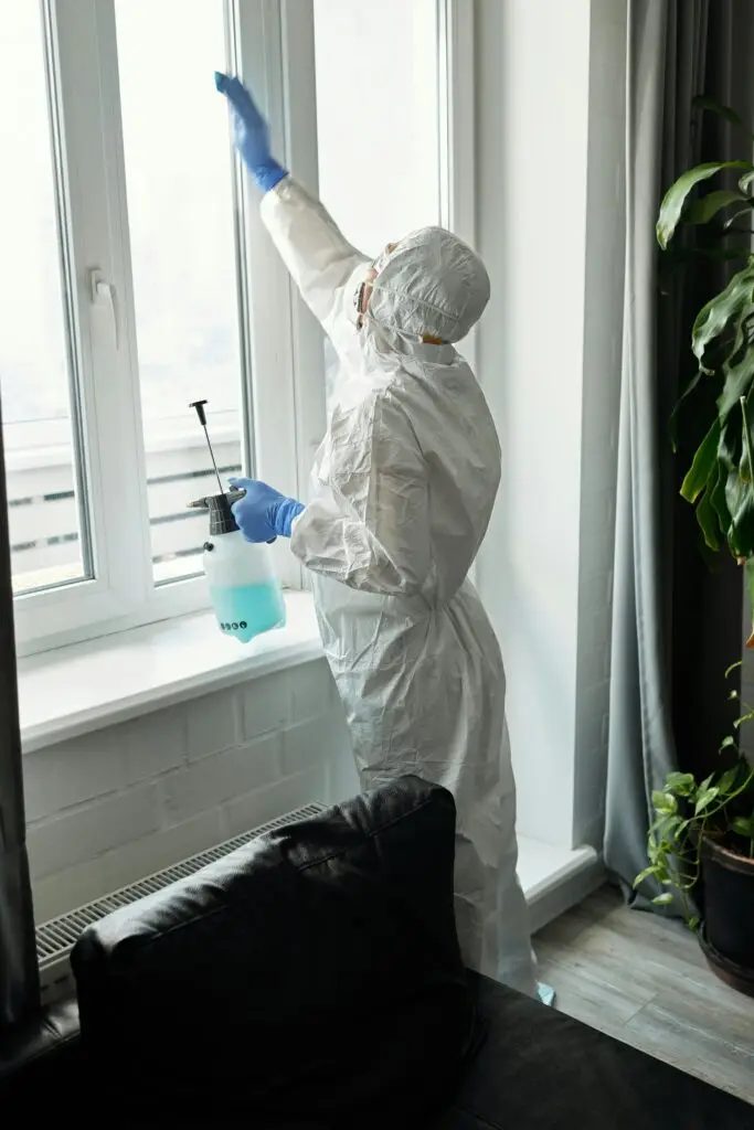 Person in full PPE cleaning an indoor glass window, ensures hygiene.