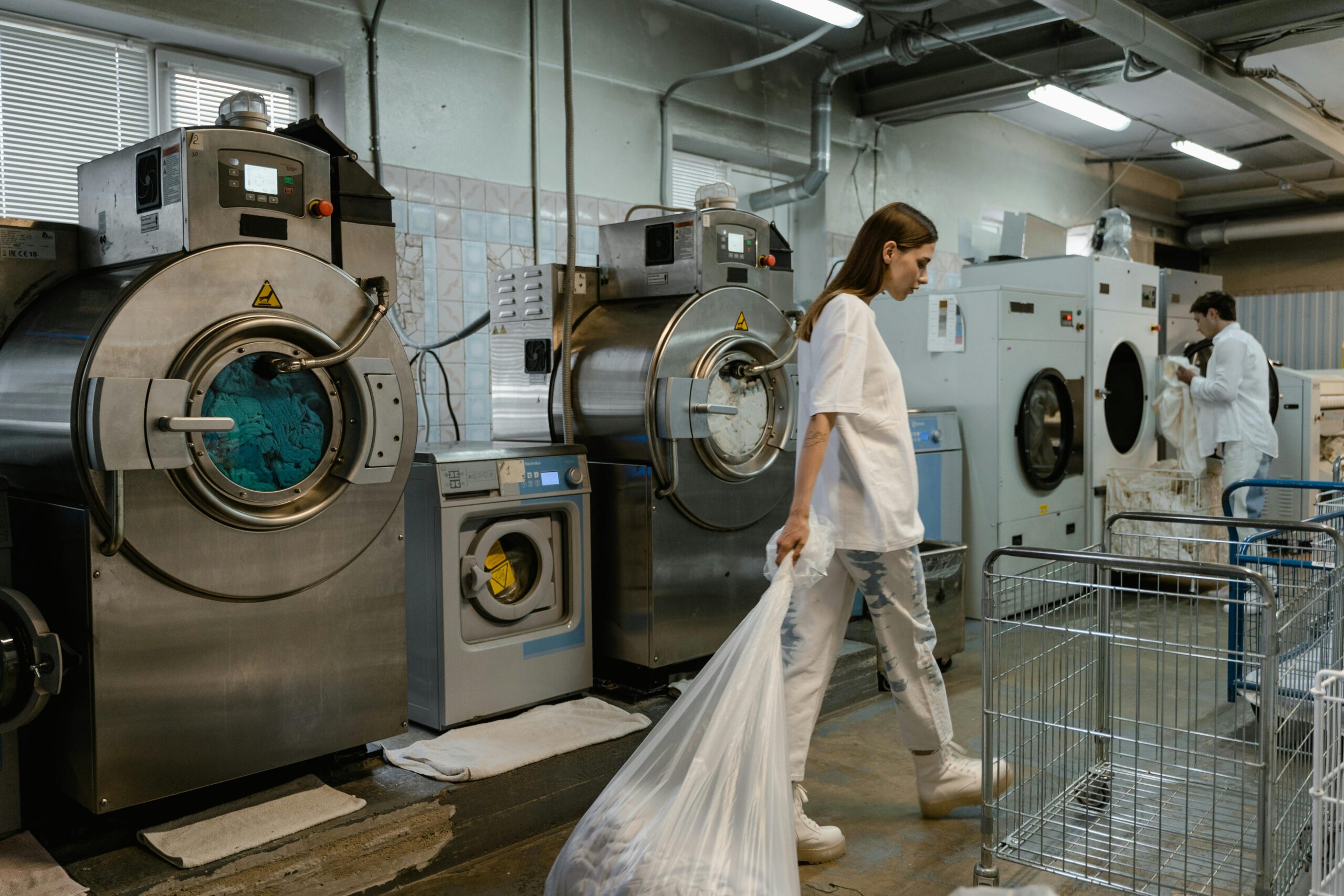 Busy industrial laundry with workers handling large washing machines.