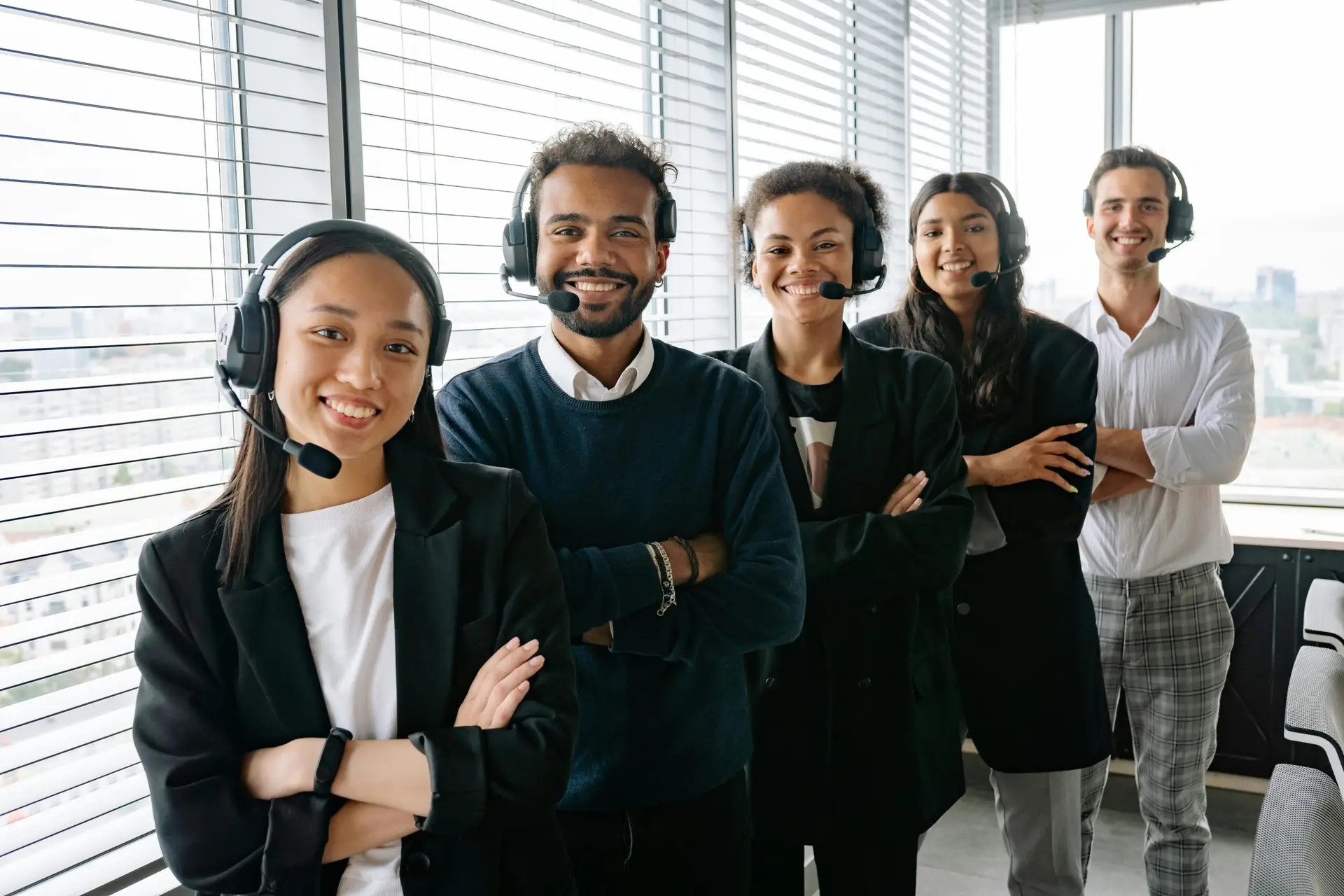 A cheerful, diverse team with headsets posing in a bright office environment.